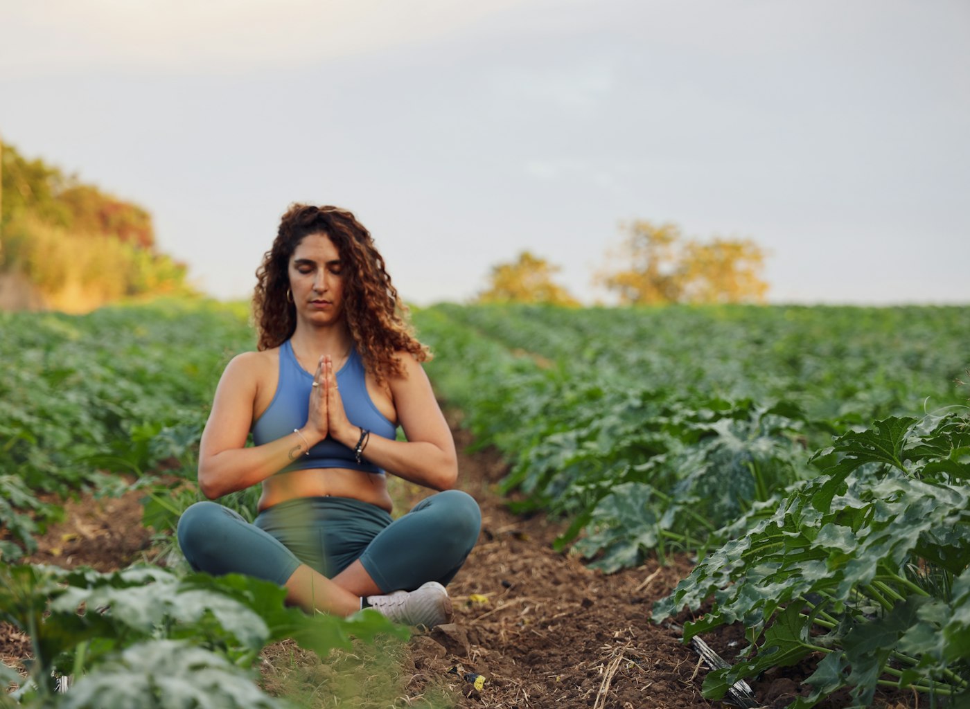 Woman of color sitting in quiet meditation outdoors, surrounded by plants.